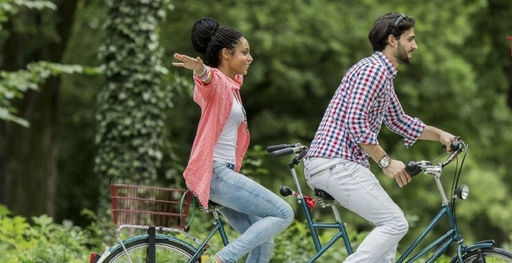Couple on a tandem. She is on the back seat with her arms outstretched